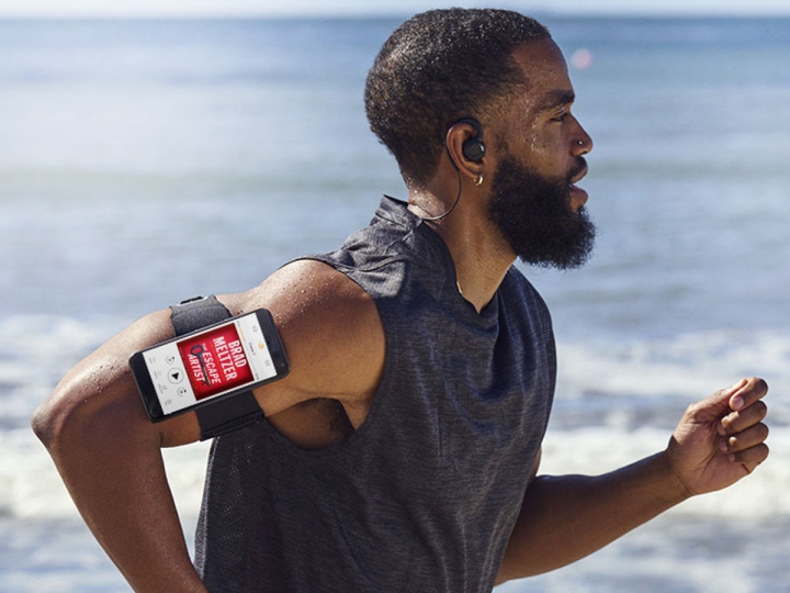 مردی در امتداد ساحلی می دود که یک گوشی هوشمند کتاب صوتی را به بازویش نشان می دهد.