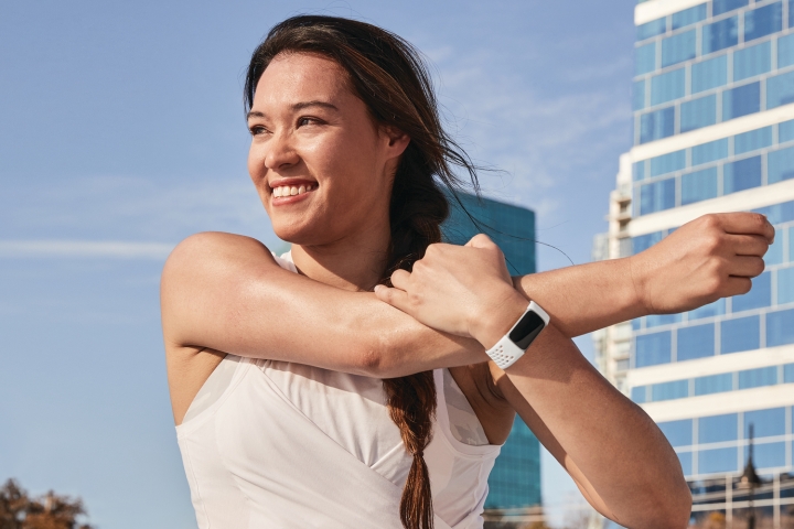 زنی که در فضای باز لبخند می زند با لباس ورزشی و Fitbit Charge 5 روی مچ دستش.
