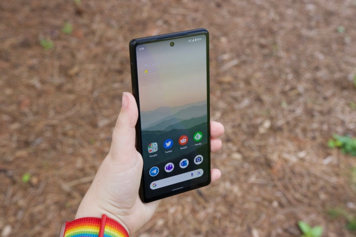 شخصی یک Google Pixel 6a در دست دارد.  صفحه نمایش روشن است و صفحه اصلی گوشی را نشان می دهد.