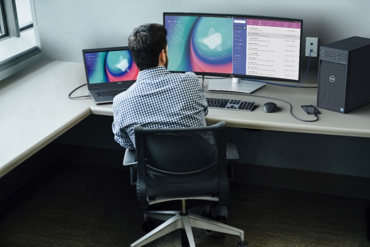 مردی پشت میز کار می کند در مقابل یک مانیتور منحنی Dell UltraSharp 34 که به یک لپ تاپ متصل است.